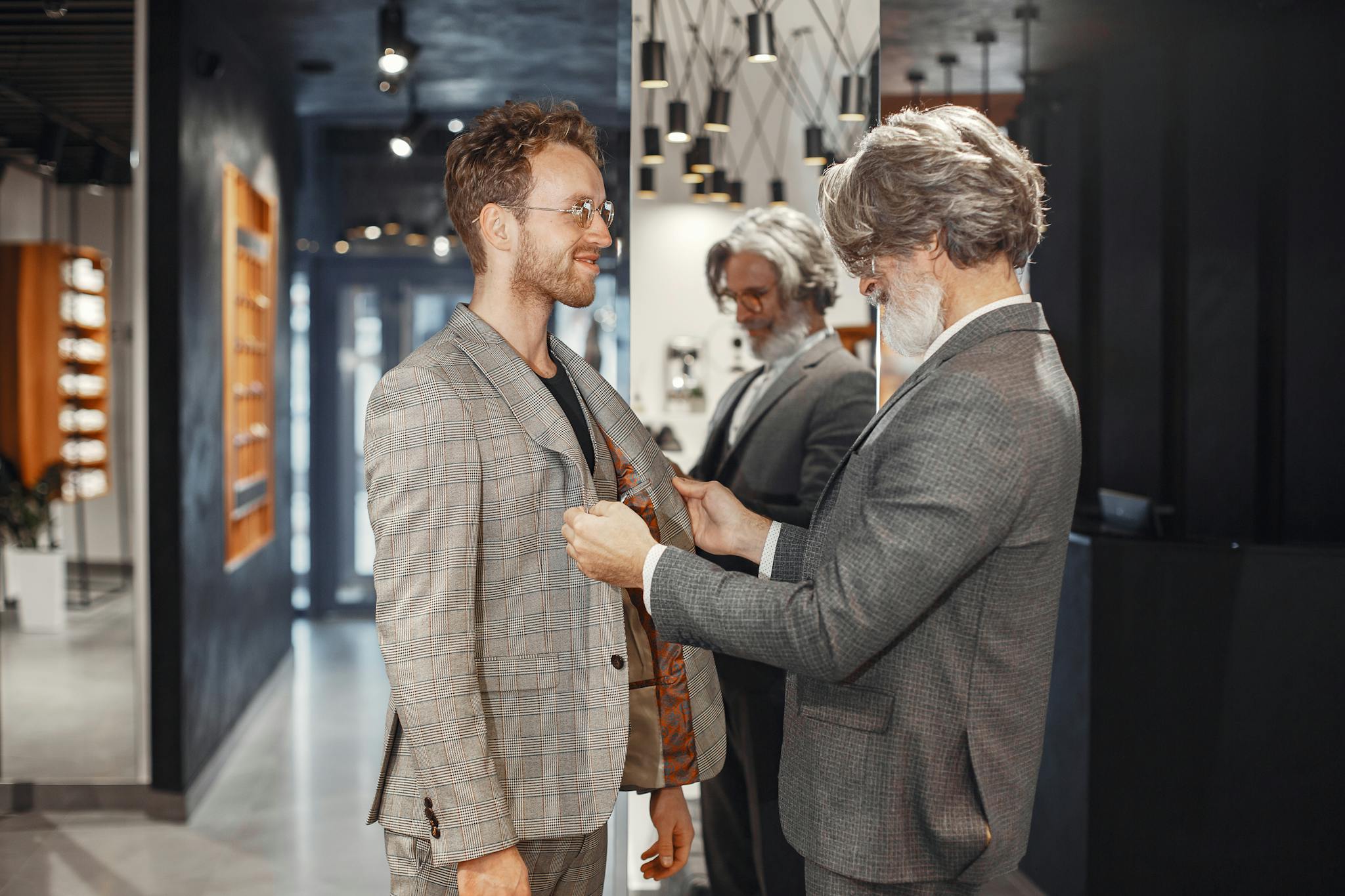 A tailor adjusts a customer's suit jacket in a stylish, modern boutique store setting.