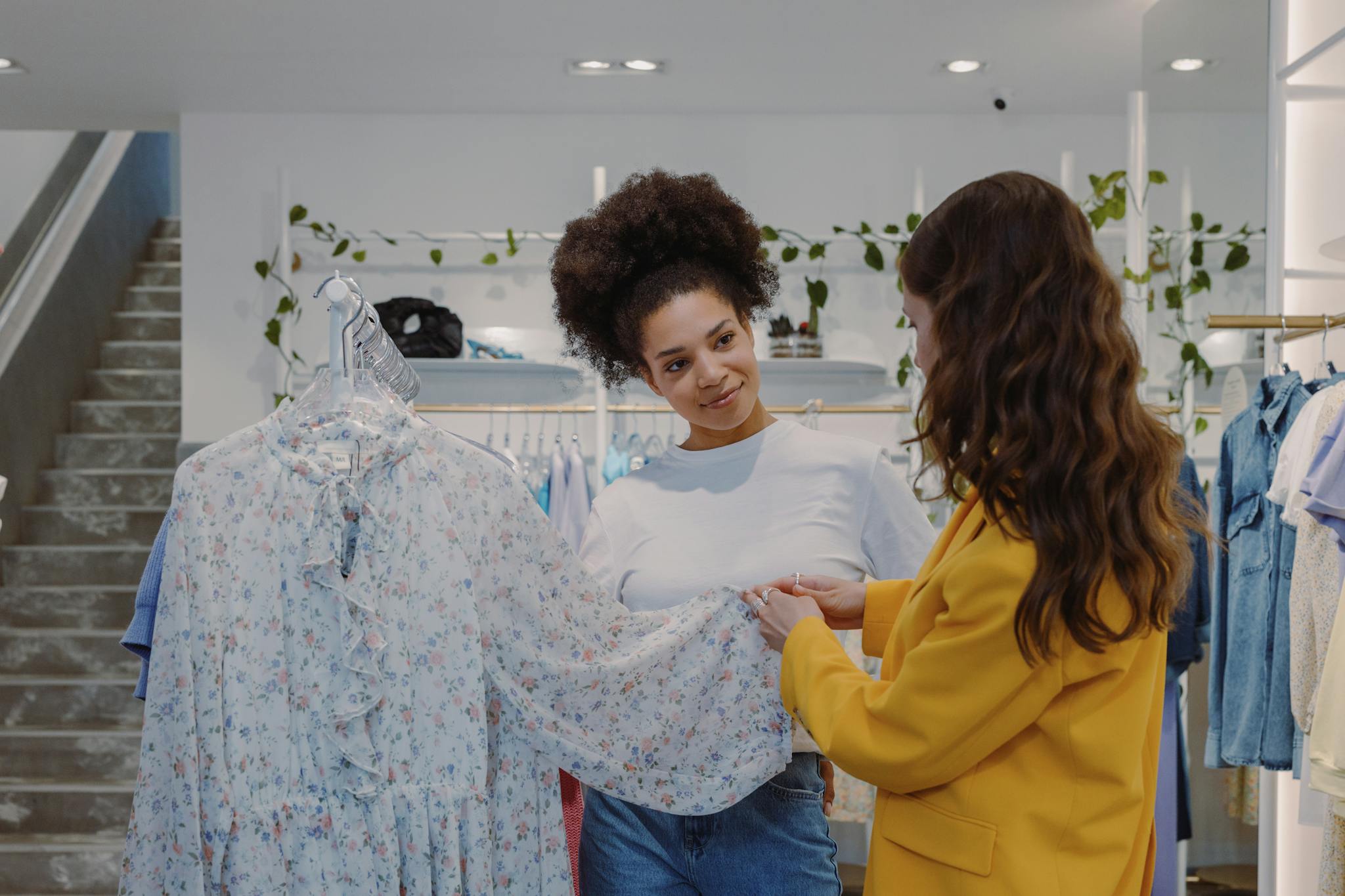 Two women exploring floral dresses in a trendy boutique setting, enjoying a shopping experience.
