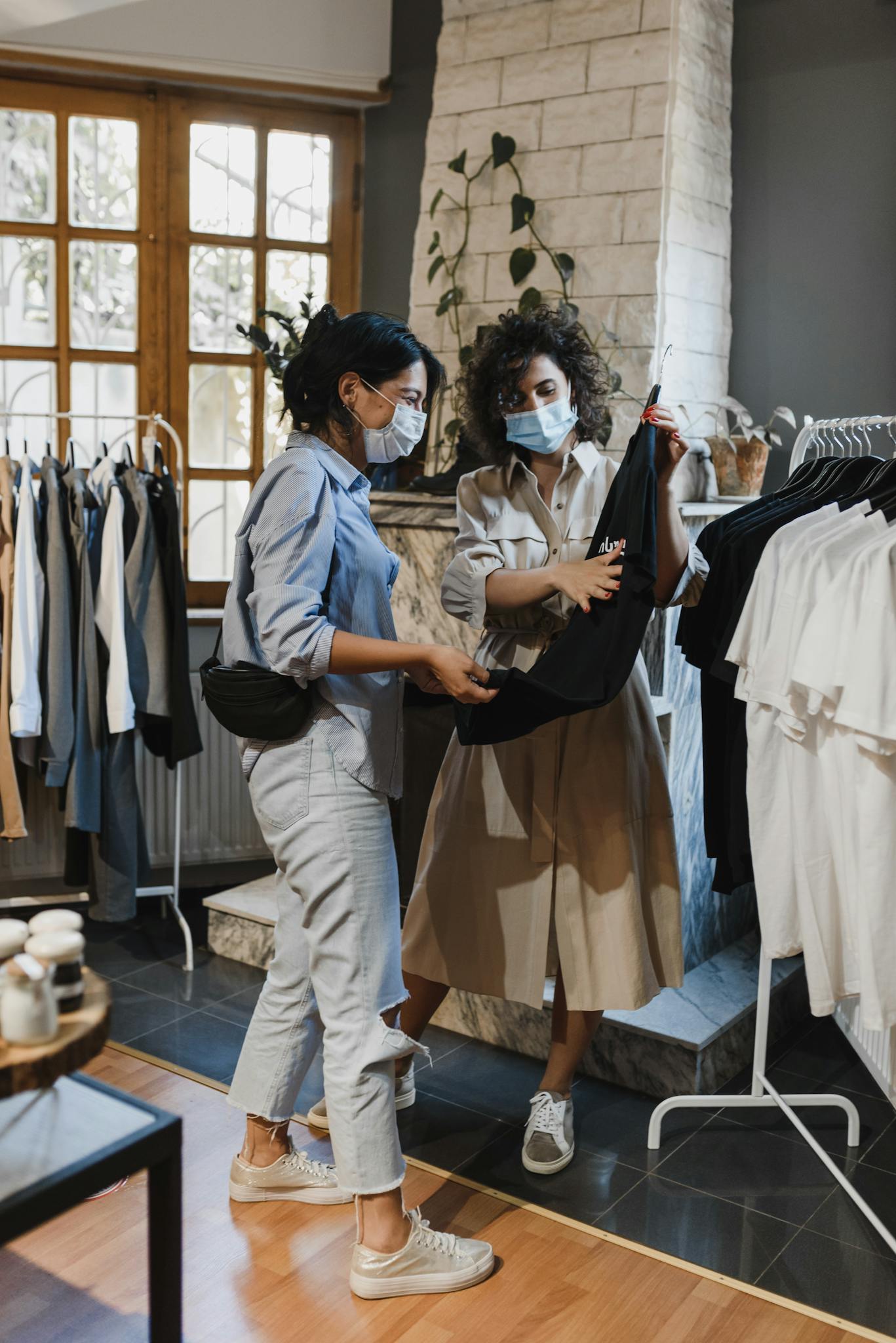Two women wearing masks shop for clothes in a boutique during pandemic.